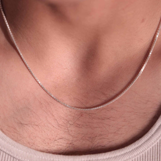 A close-up of a 925  sterling silver box chain necklace on a mens chest.