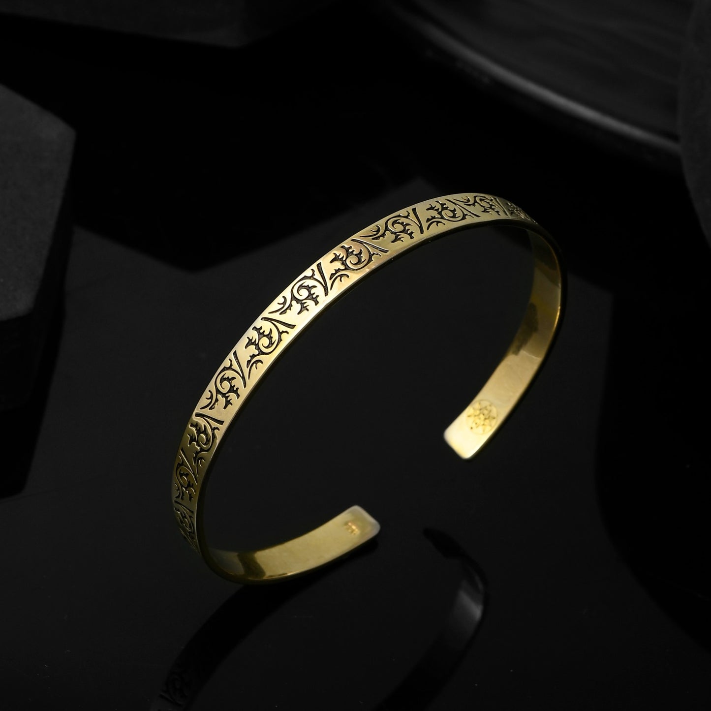 This image showcases a mens gold cuff bracelet, its surface adorned with an intricate floral pattern.