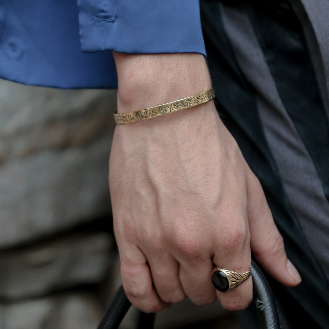 A gold cuff bracelet with a beautiful floral design wraps around mens wrist