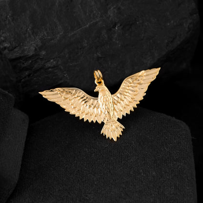 A gold eagle pendant for men shaped like a bird of prey with a curved beak and sharp talons is placed on a black rock.