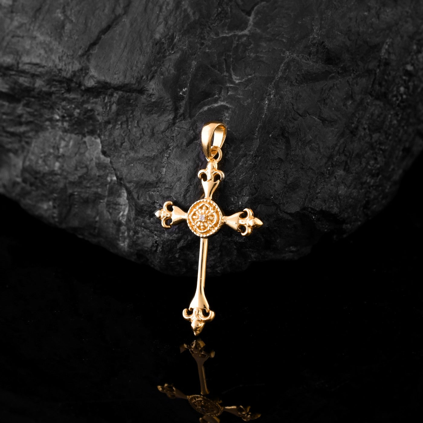 A close-up view of a gold Jesus cross pendant for men, set with a sparkling diamond in the center. The pendant sits on top of a rough, black rock.