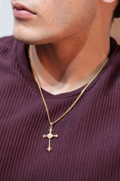 Combining religious and symbolic elements, a gold cross pendant incorporates a fleur-de-lis motif. The pendant hangs from a gold chain