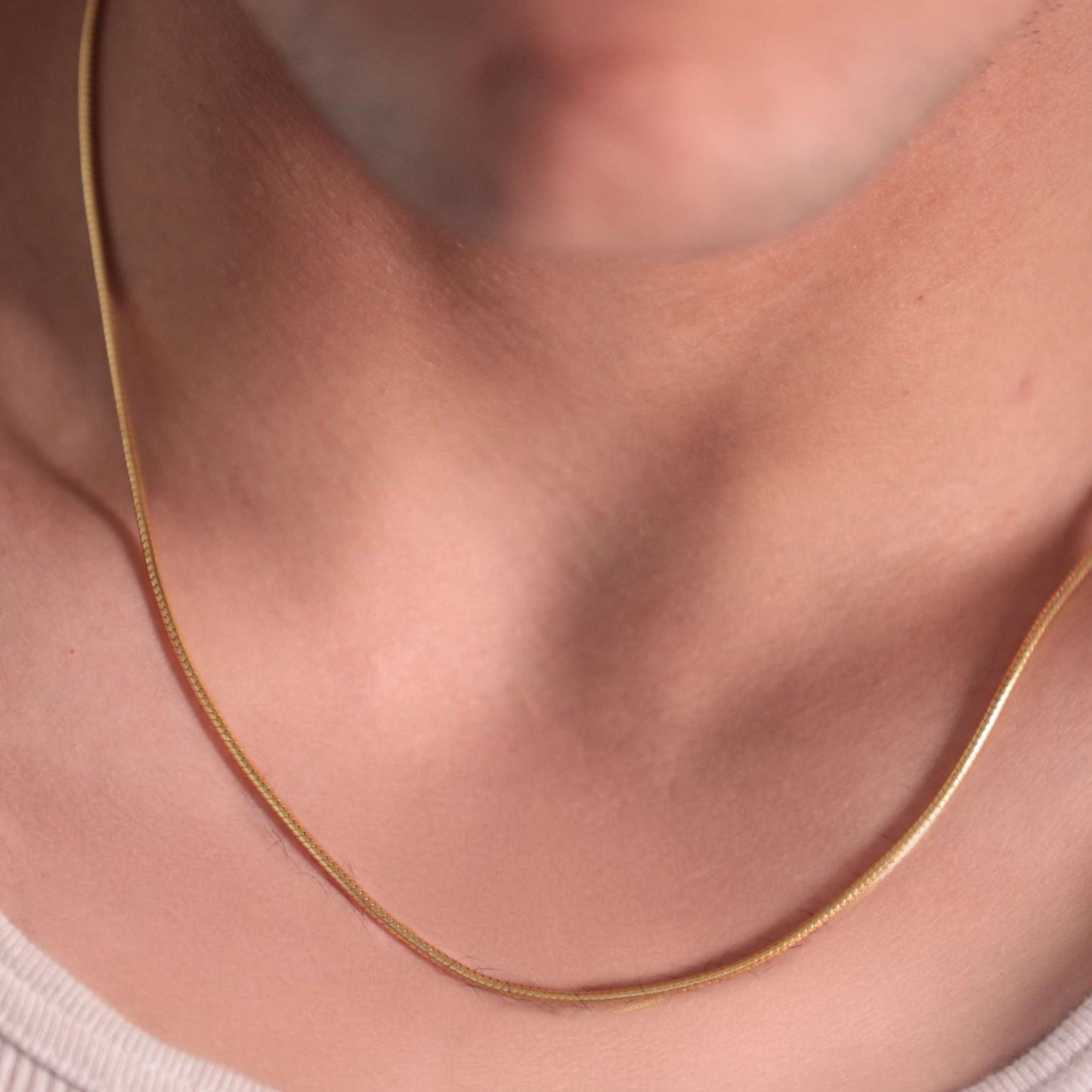 Man's gold snake chain necklace takes center stage in this close-up. The polished metal reflects light, showcasing a bold and eye-catching design.